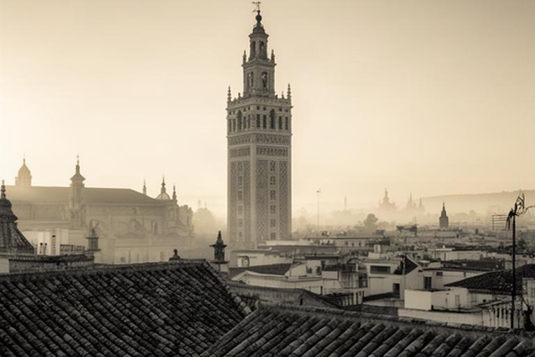 Giralda de Sevilla al amanecer vista entre tejados, con luz suave sobre el perfil histórico de la ciudad